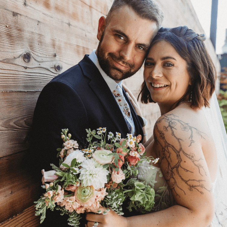 Bride and Groom looking at camera with bridal bouquet between them in pinks and whites